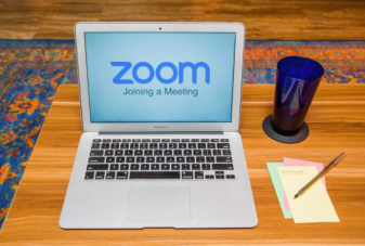 macbook with zoom logo with pens, notepad on wooden desk on rug